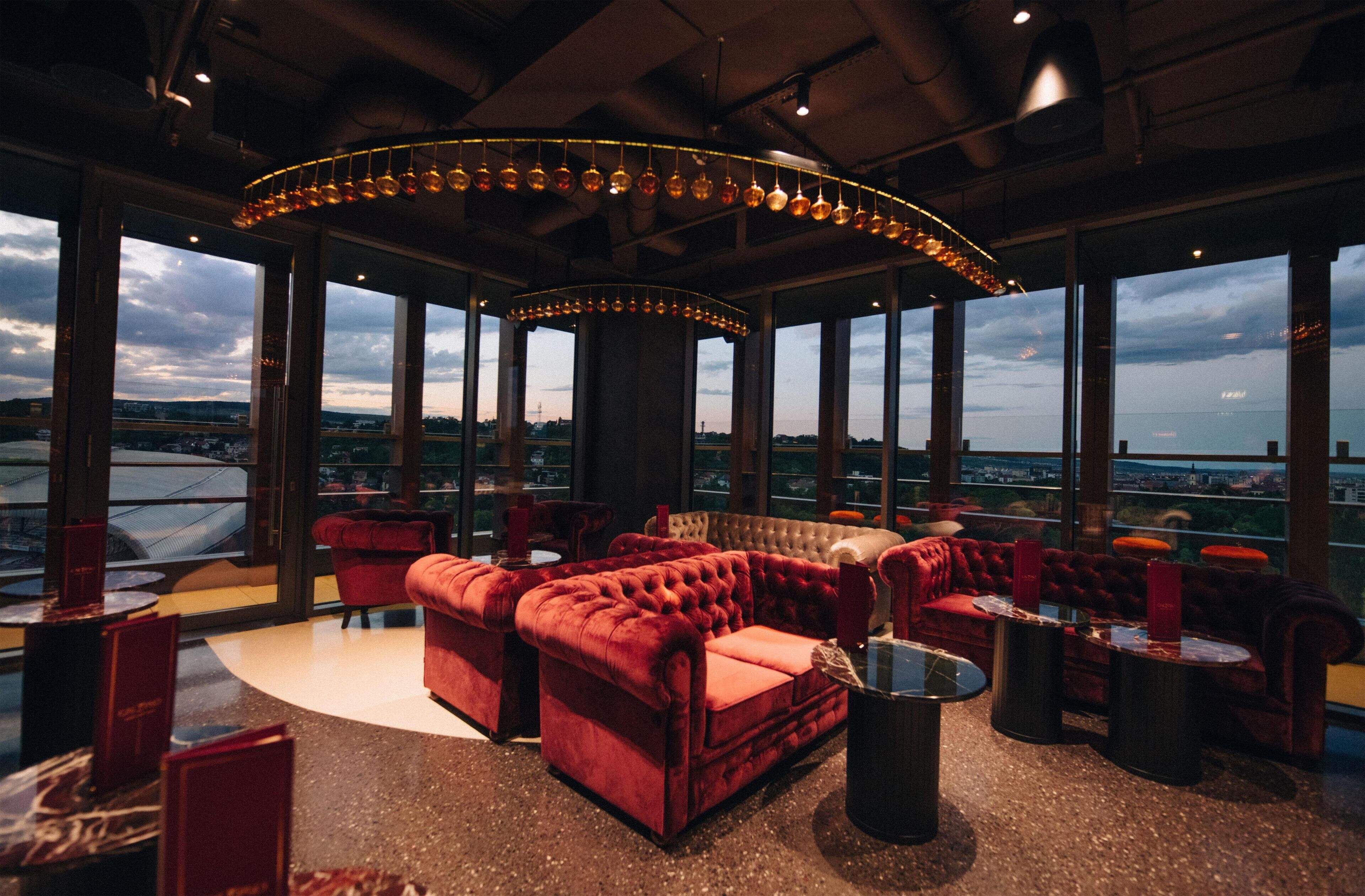 A high-ceiling lounge with a circular seating area, large windows, and a city view.