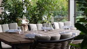A dining table set with plates, glasses, and a water glass, surrounded by cushioned chairs, with large windows and greenery in the background. - Radisson Blu Hotel, Cluj (Cluj-Napoca)