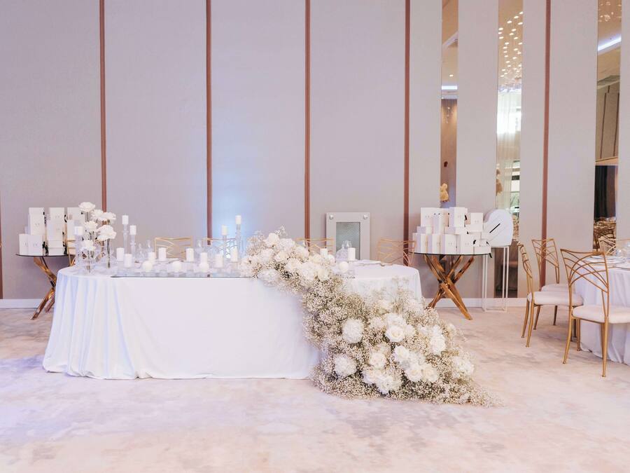 A wedding reception setup with a white table, floral arrangements, and gold chairs.