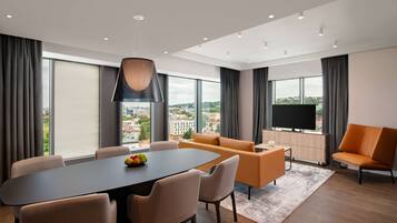Una sala de estar moderna con comedor, ventanas amplias, televisor de pantalla plana y vista a la ciudad.