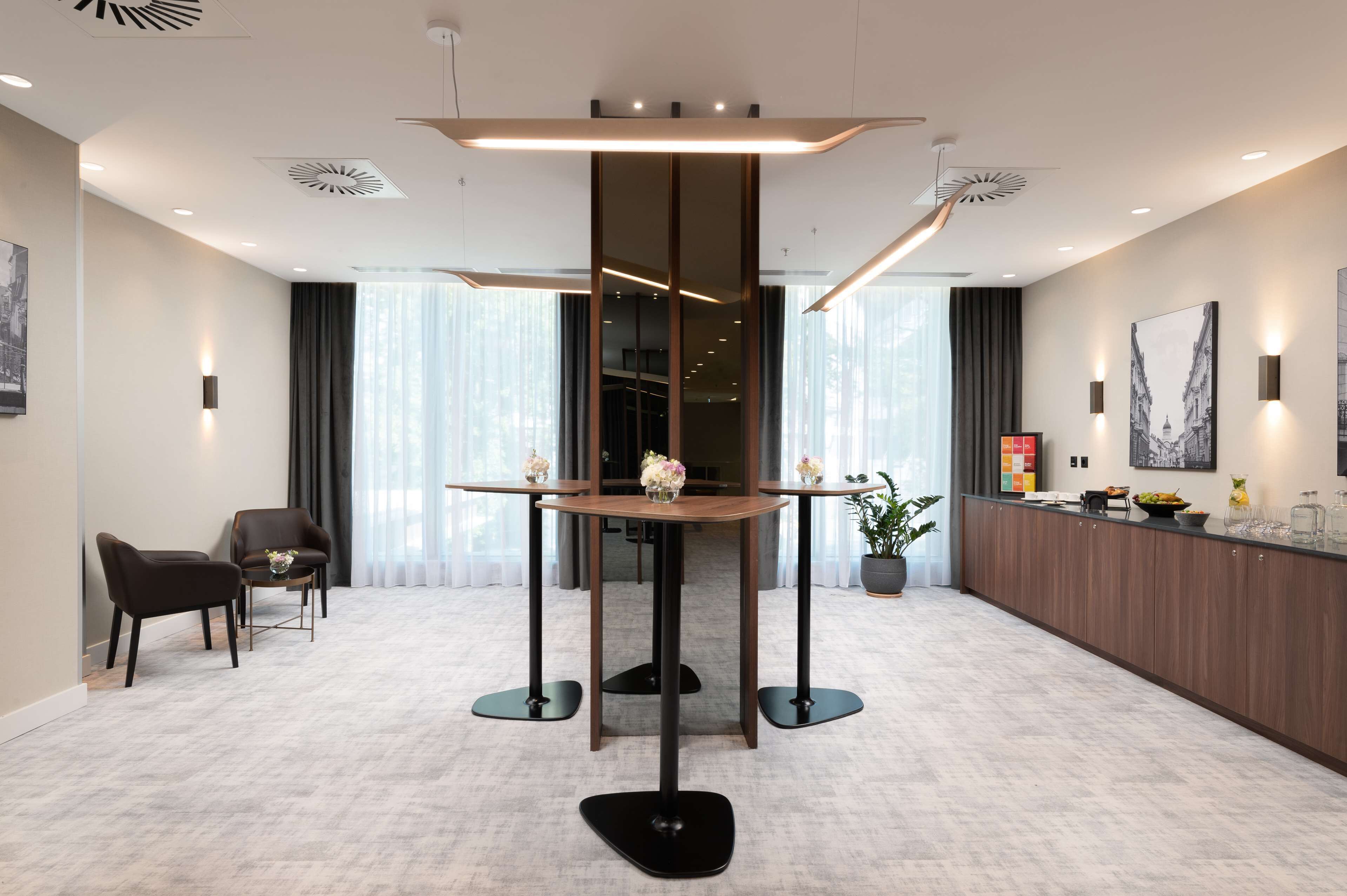 Un hall d’hôtel moderne avec une table centrale, deux chaises, un comptoir d’accueil et de grandes fenêtres dotées de rideaux.