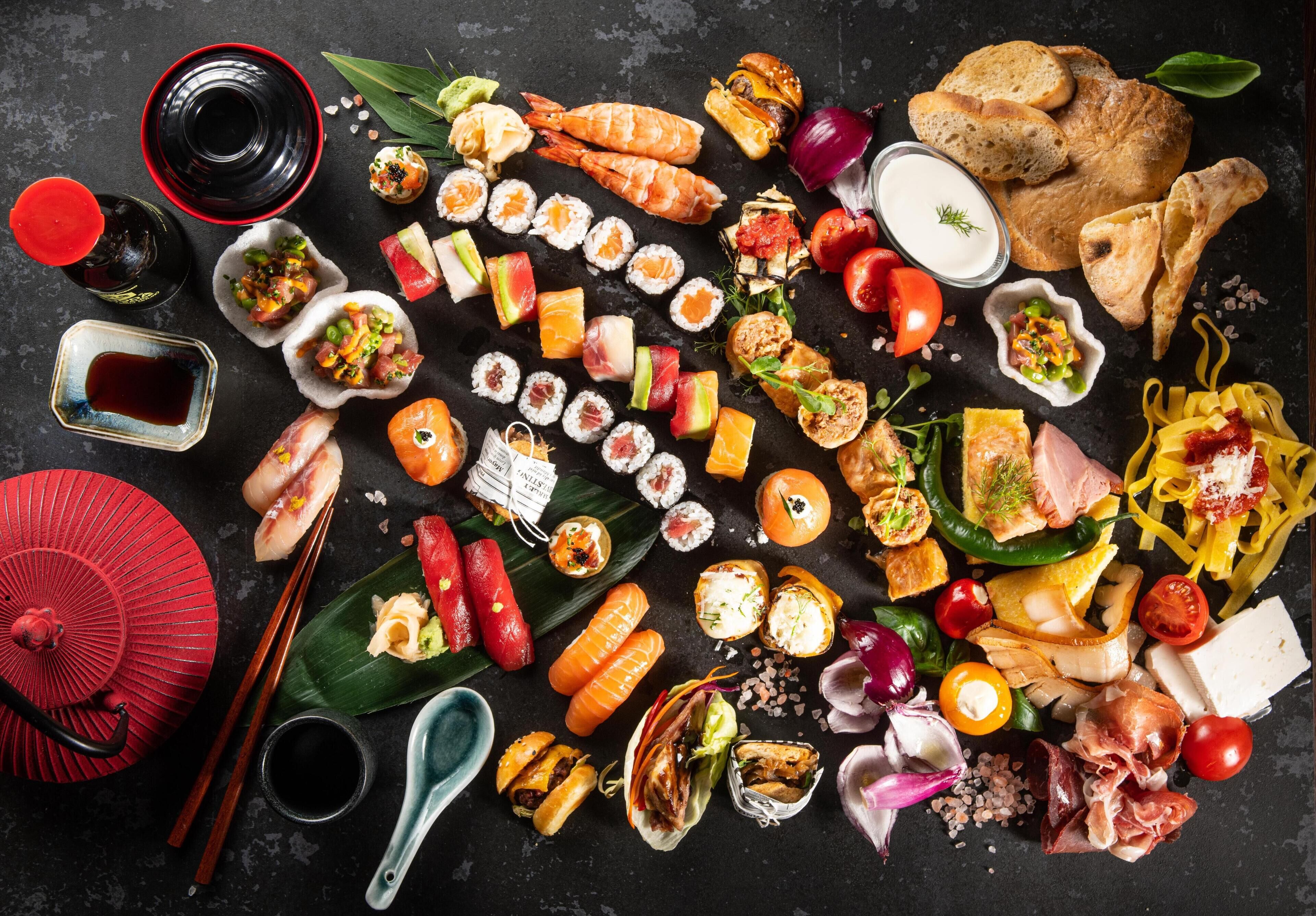 Une variété de plats de sushis et de sashimis, notamment des rouleaux et des nigiris, disposés sur une surface sombre, accompagnés de baguettes, d’un éventail rouge et de petits bols de sauce soja.