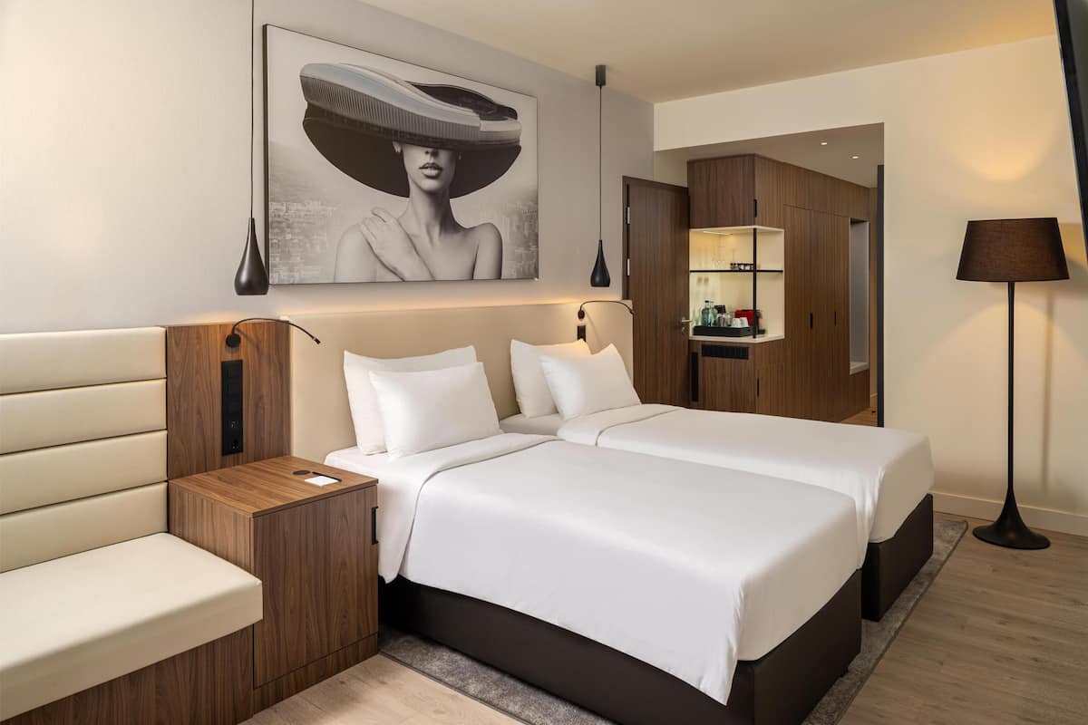 Quarto de hotel com cama de casal, mesa de cabeceira, luminária, guarda-roupa e um quadro na parede.