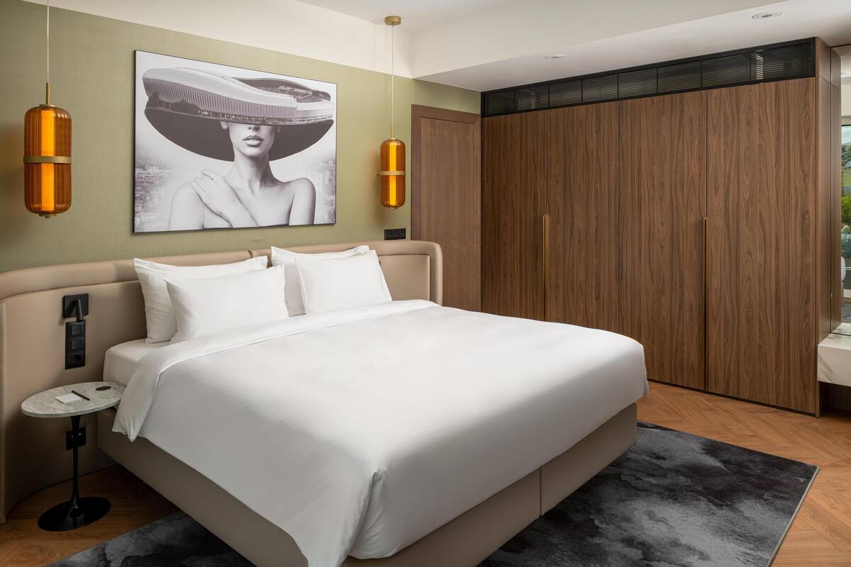 Quarto moderno com cama grande, mesa de cabeceira, guarda-roupa e uma obra de arte na parede.