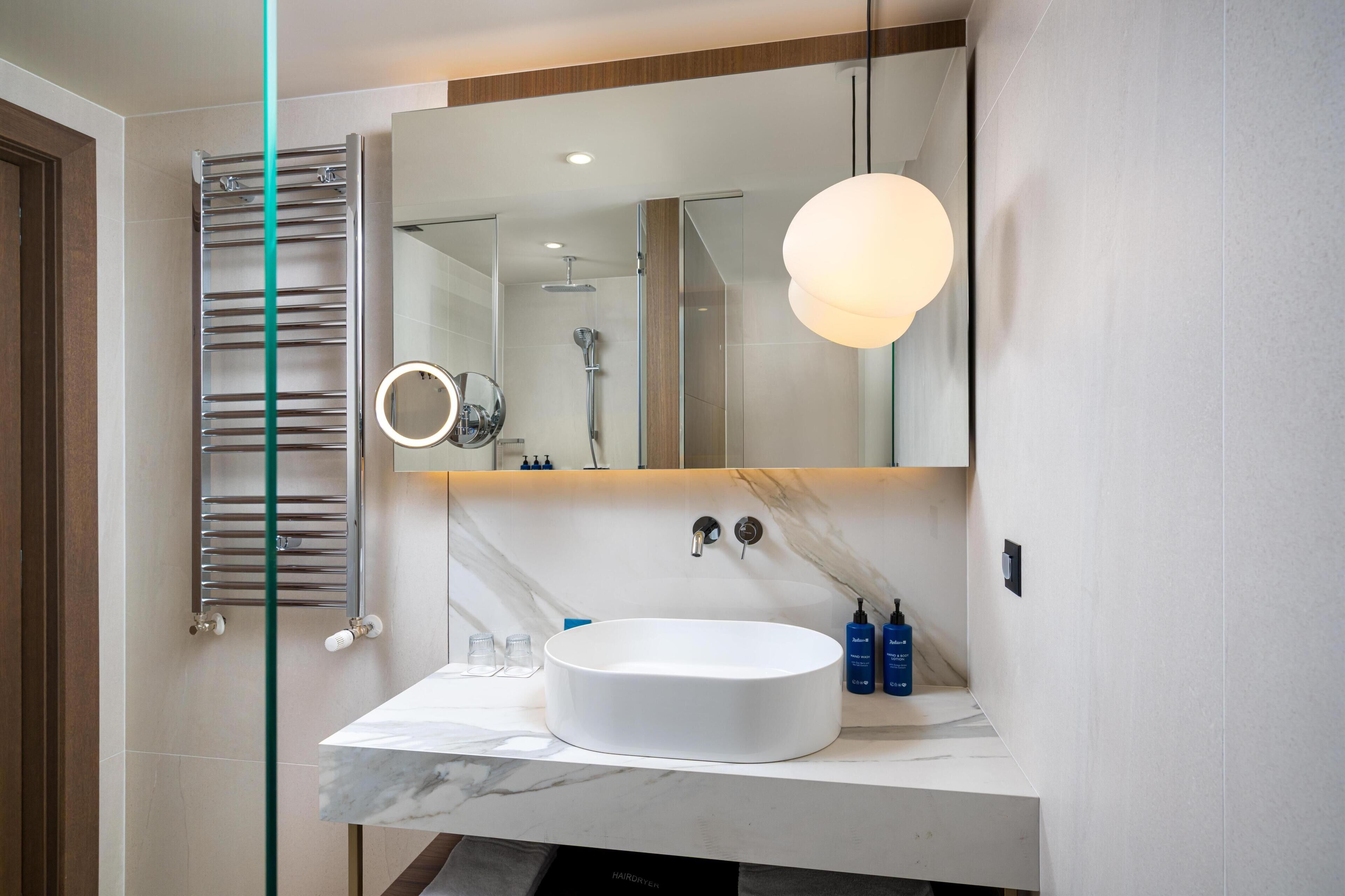 A modern bathroom with a round sink, a mirror, a towel rack, and a shower.