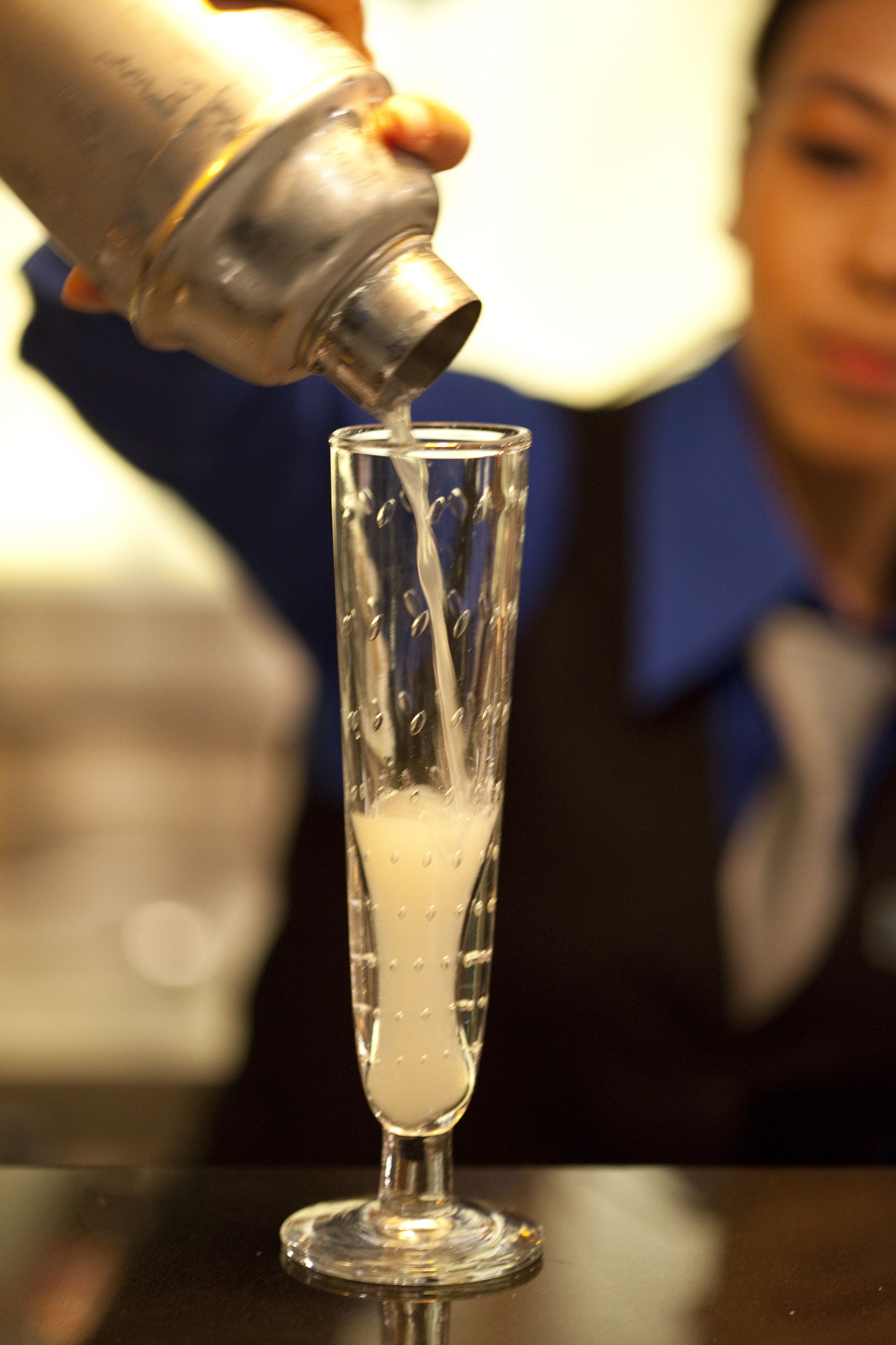 A person pouring a liquid from a bottle into a tall glass.