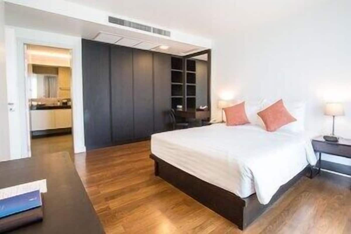 A modern bedroom with a large bed, a dark wardrobe, and a small bedside table with a lamp.