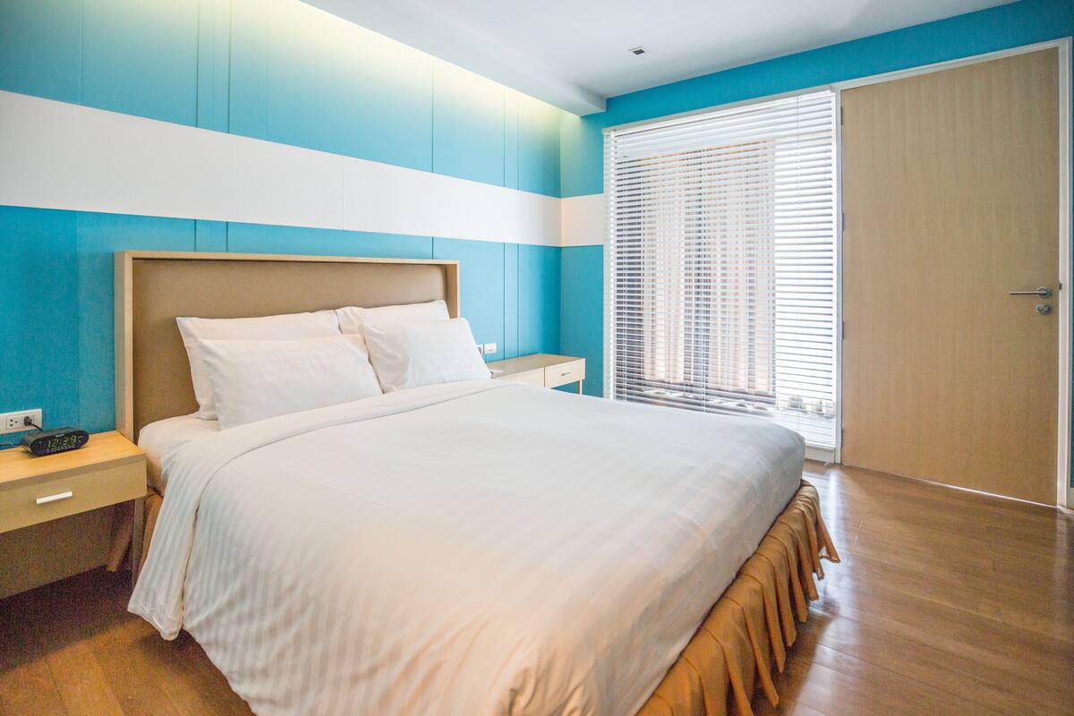 A bedroom with a bed, bedside table, and a window with blinds.