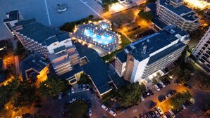 An aerial view of a hotel with a swimming pool, multiple parking lots, and surrounding buildings. - Orfeu (Constanta)