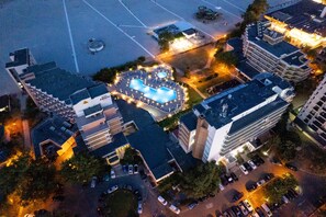 An aerial view of a hotel with a swimming pool, multiple parking lots, and surrounding buildings. - Orfeu (Constanta)