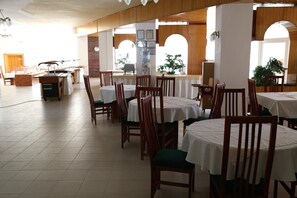 A spacious dining area with multiple tables and chairs, wooden paneling, and large windows allowing natural light.