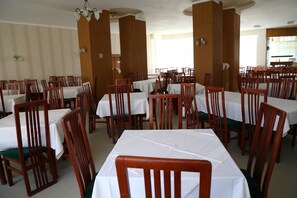 Un comedor con varias mesas y sillas, paneles de madera y una araña.