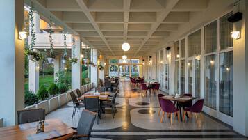 A covered outdoor dining area with tables and chairs, hanging plants, and large windows.