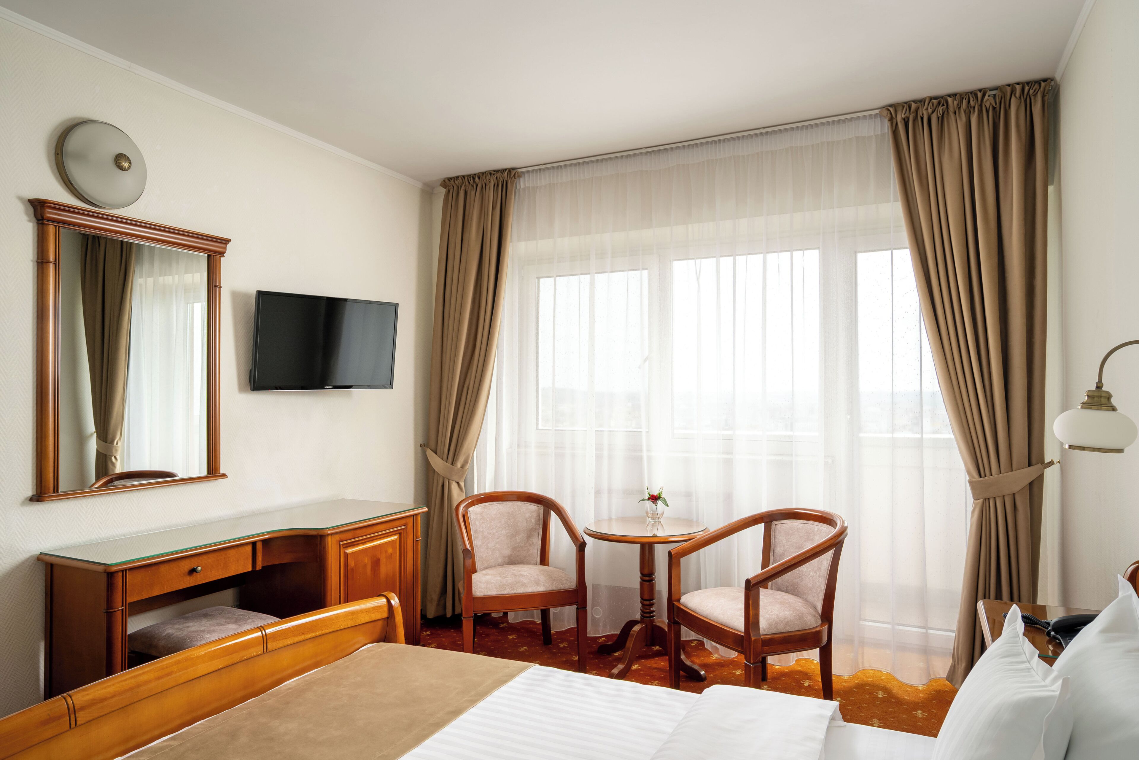 A hotel room with a bed, a desk, a chair, a television, and a window with curtains.