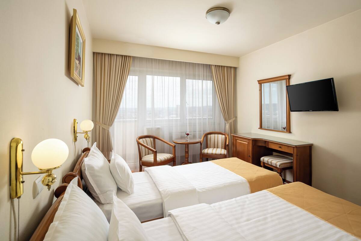 A hotel room with two beds, a desk, a chair, a television, and a window with curtains.