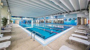Una piscina interior con varias pistas, suelo de baldosas y techo con vigas lineales.