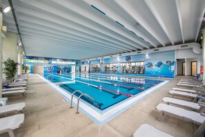 An indoor swimming pool with multiple lanes, a tiled floor, and a ceiling with linear beams. - Hotel Belvedere (Cluj-Napoca)