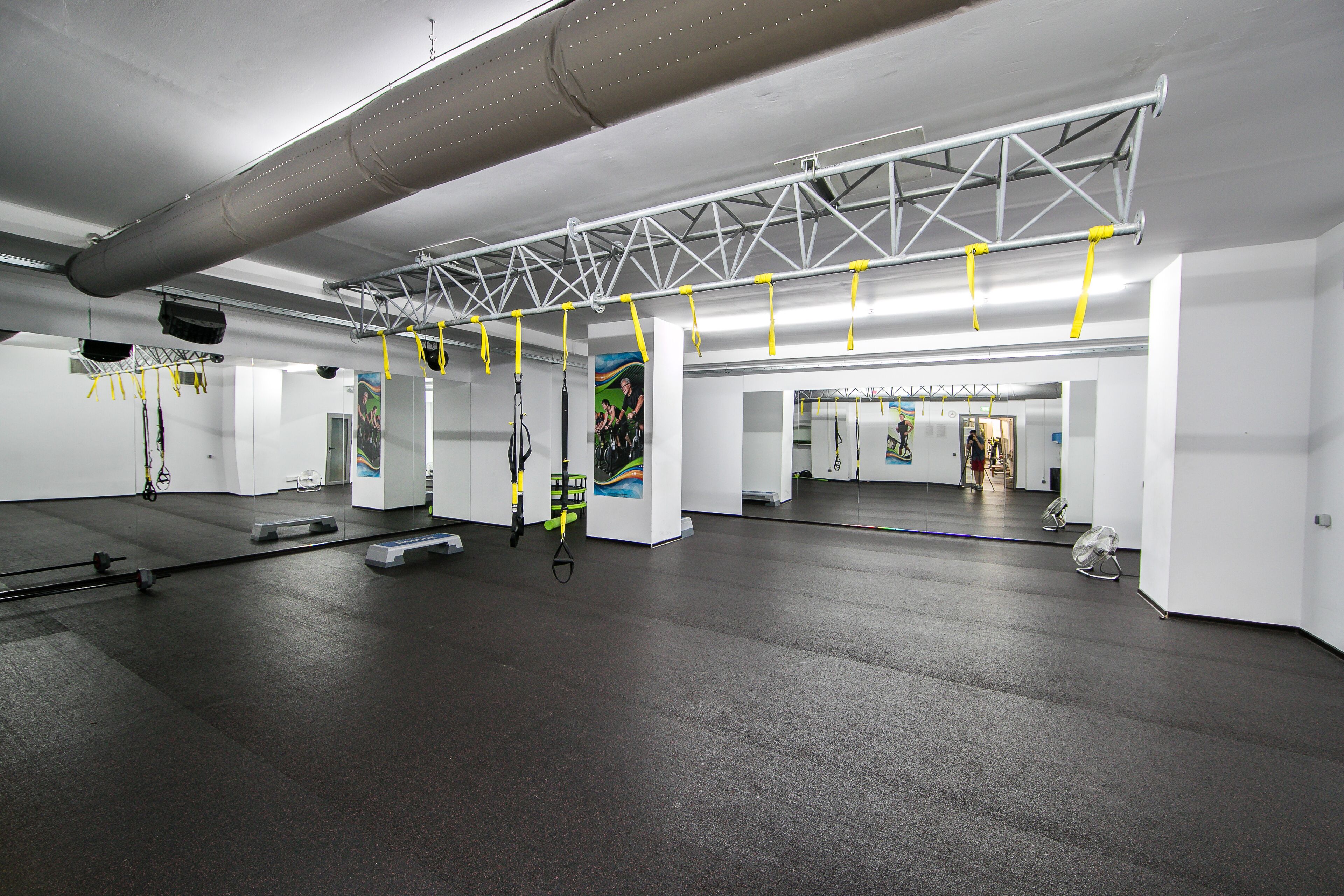 A spacious indoor area with a high ceiling, metal truss structure, and suspended exercise equipment.