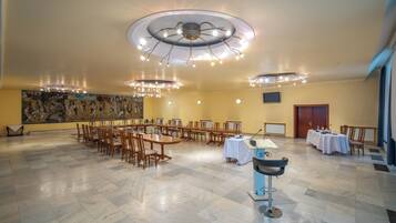 Une salle de conférence avec des tables et des chaises rondes, une grande fresque murale et un plafond doté de plusieurs luminaires.