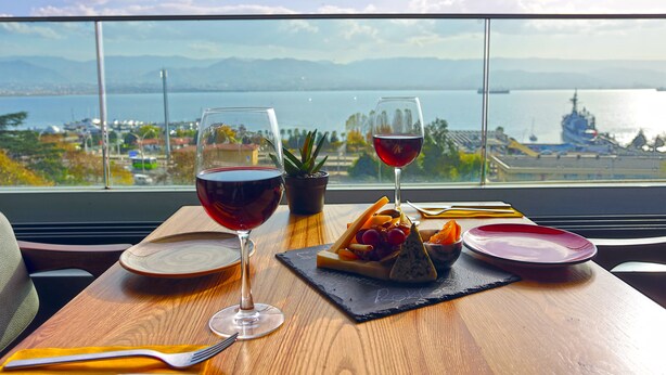 A table with a meal and wine glasses, a view of a body of water and a ship, and a potted plant. - Wes Hotel Izmit (Izmit)