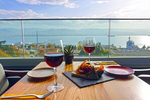 A table with a meal and wine glasses, a view of a body of water and a ship, and a potted plant.