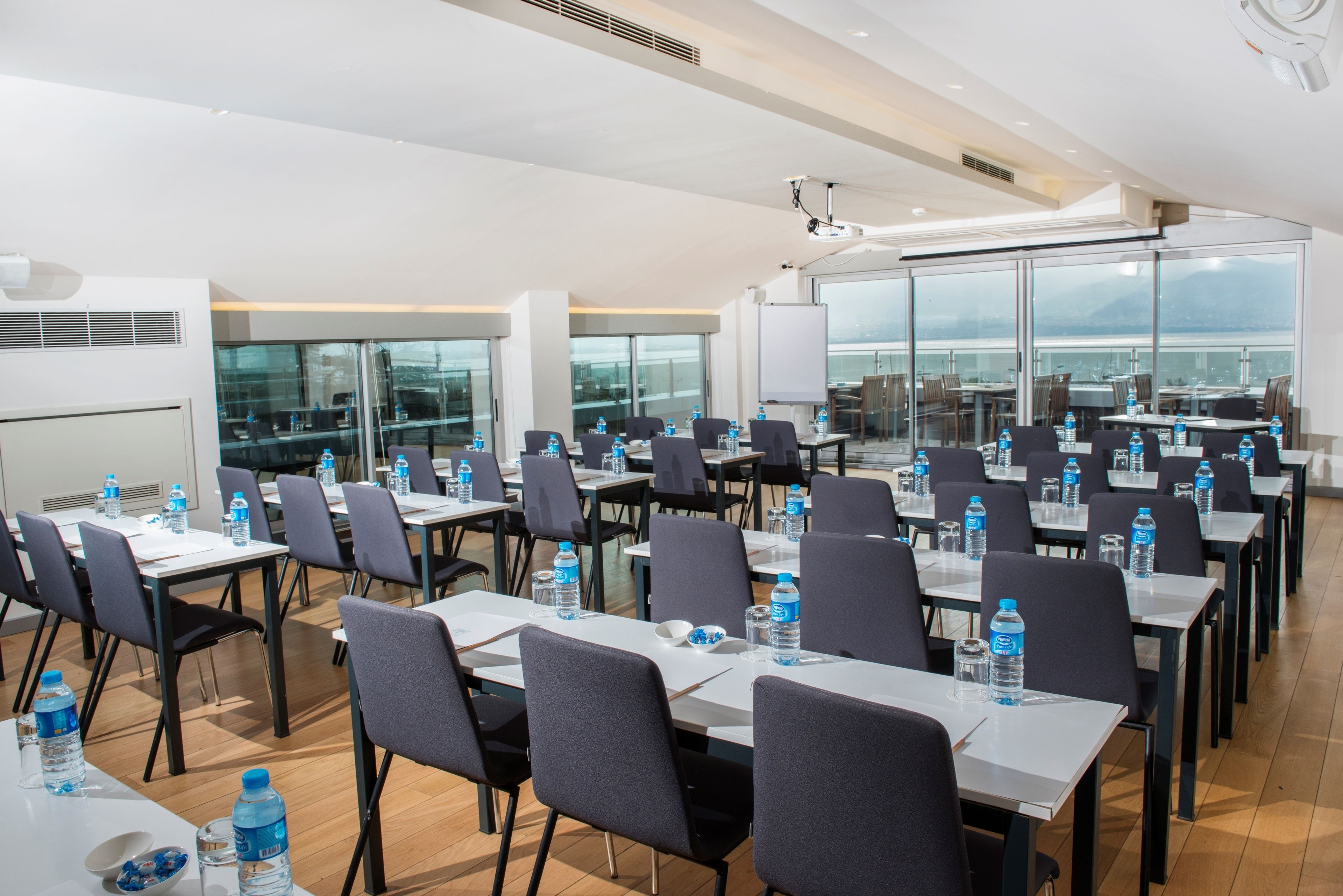 A conference room with multiple tables and chairs, equipped with water bottles and a whiteboard.