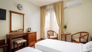 A hotel room with two beds, a desk with a chair, a small table with a chair, a mirror, and an air conditioning unit. - Sarmis (Deva)