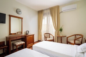 A hotel room with two beds, a desk with a chair, a small table with a chair, a mirror, and an air conditioning unit. - Sarmis (Deva)