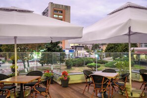An outdoor seating area with tables and chairs, potted plants, and a view of the street. - Sarmis (Deva)