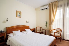 A hotel room with a bed, two chairs, a small table with a vase, and an air conditioning unit. - Sarmis (Deva)