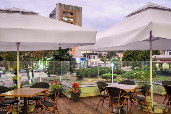 An outdoor seating area with tables and chairs, potted plants, and a view of the street.
