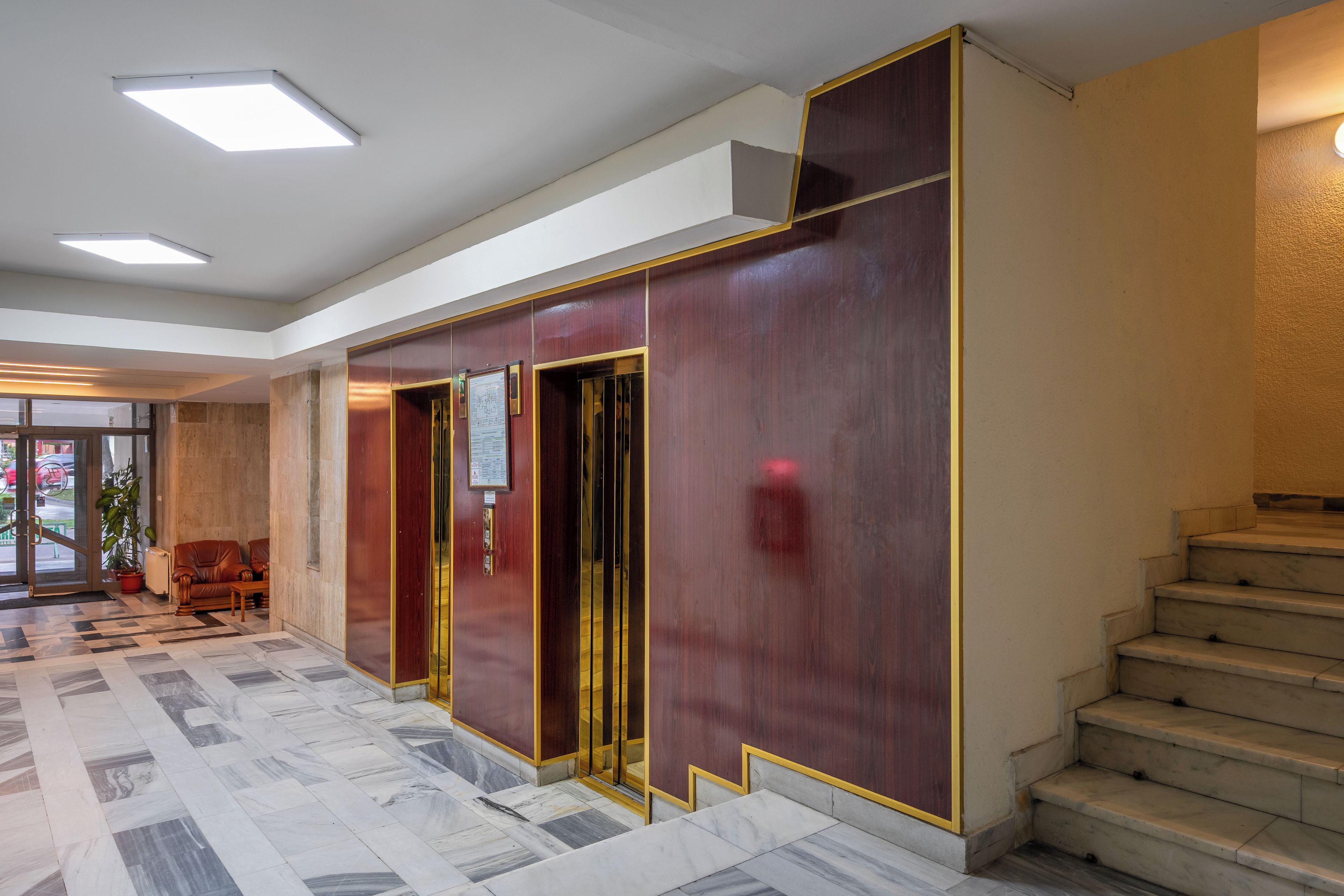 A lobby with a marble floor, a staircase, and a reception area with a desk and chairs.