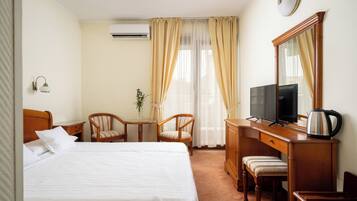 Habitación de hotel con cama, escritorio con televisor, silla, mesita pequeña y ventana con cortinas.