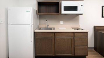 A compact kitchen with a white refrigerator, a microwave, and wooden cabinets.