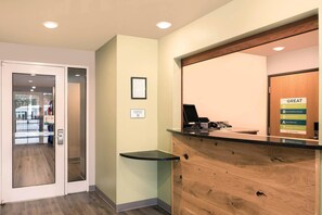 A reception desk with a computer, a phone, and a sign about the hotel's commitment to great service. - WoodSpring Suites Charlotte Gastonia (Gastonia)
