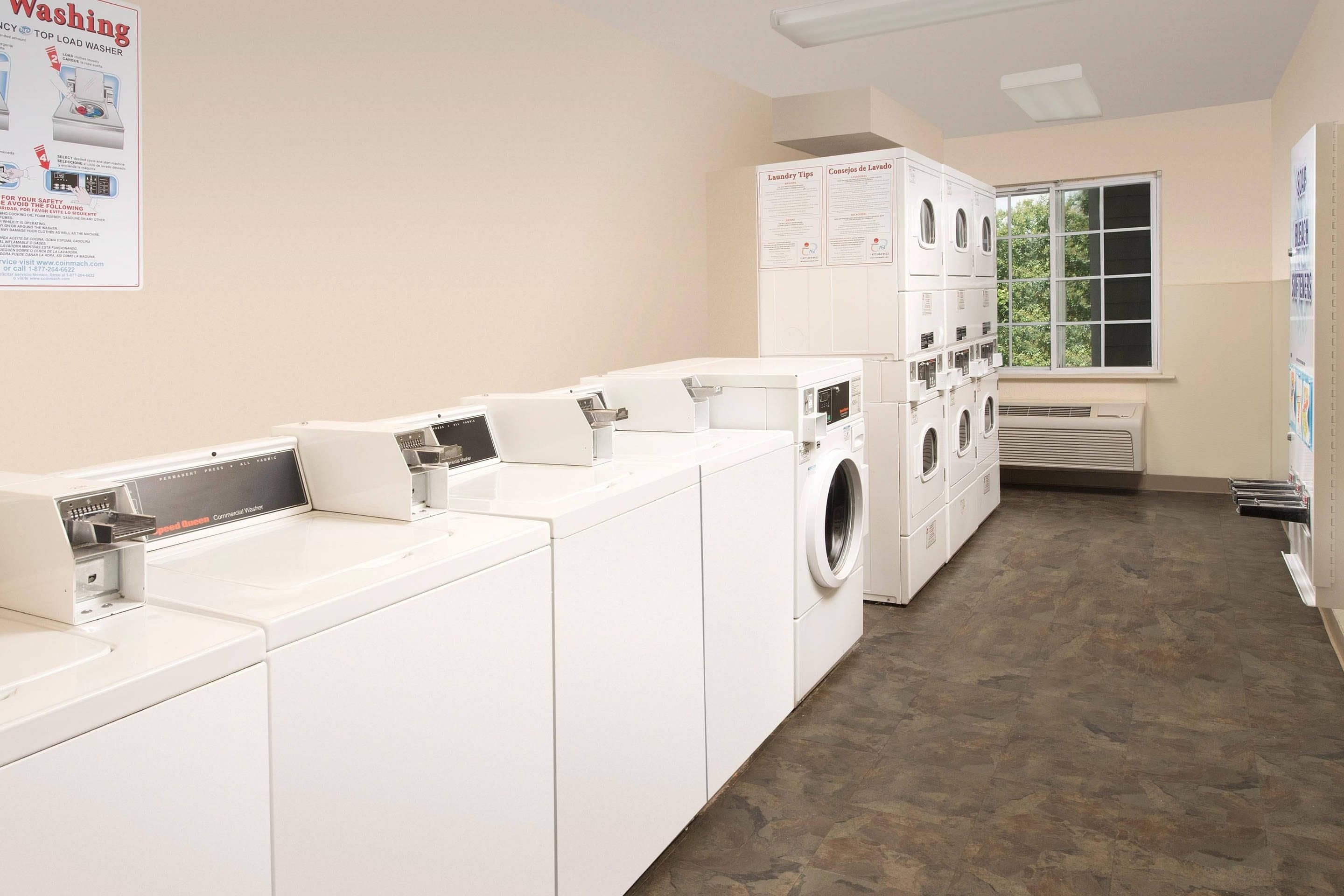 A laundry facility with multiple washing machines and dryers, a poster with laundry tips, and a window providing natural light.