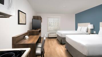 Een hotelkamer met een kitchenette, een bed, een bureau en een televisie.