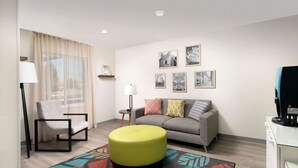 A modern living room with a sofa, a chair, a round ottoman, and a patterned rug. - WoodSpring Suites Charlotte Gastonia (Gastonia)