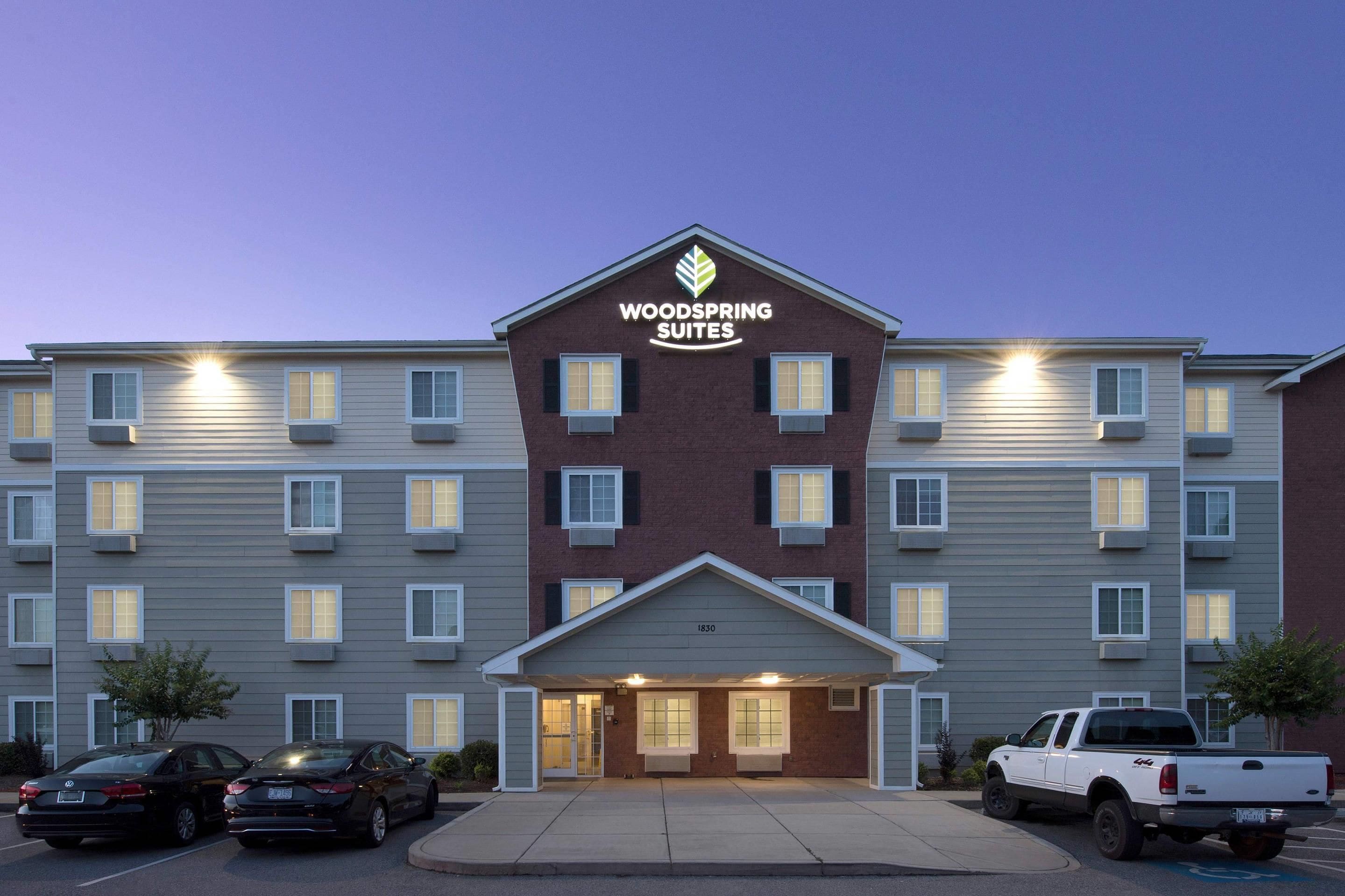 A hotel with a flat roof, multiple windows, and a sign reading 'WOODSPRING SUITES'.