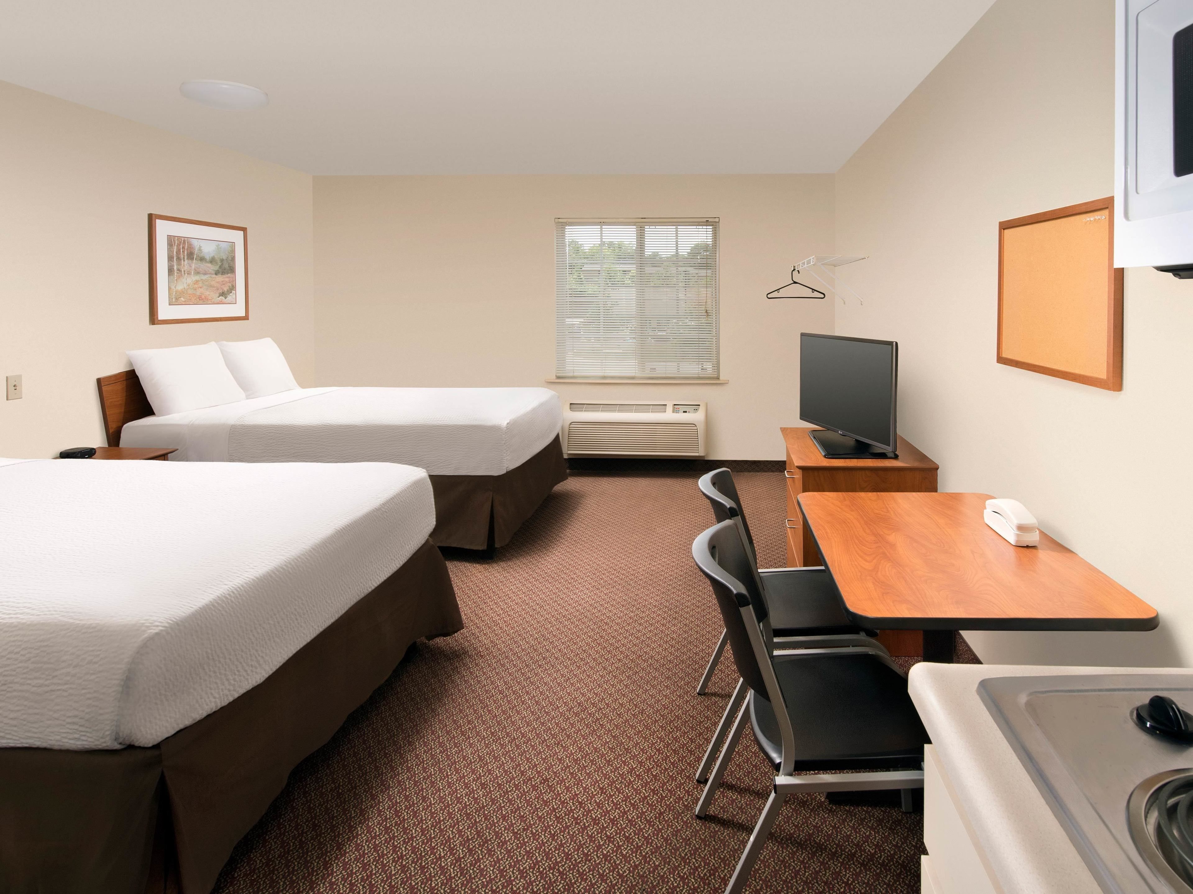 A hotel room with two beds, a desk with a chair, a television, a small table, and a sink.