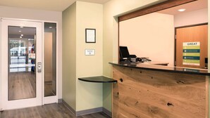 A reception area with a wooden counter, a framed sign on the wall, and a door leading to a public area. - WoodSpring Suites Charlotte Gastonia (Gastonia)