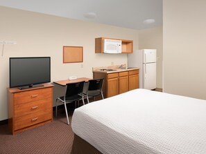 A hotel room with a bed, a desk with a TV, a microwave, a refrigerator, and a small kitchenette. - WoodSpring Suites Charlotte Gastonia (Gastonia)