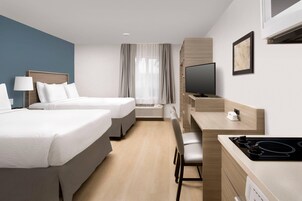 Habitación de hotel con dos camas, un escritorio, un televisor y una ventana con cortinas.