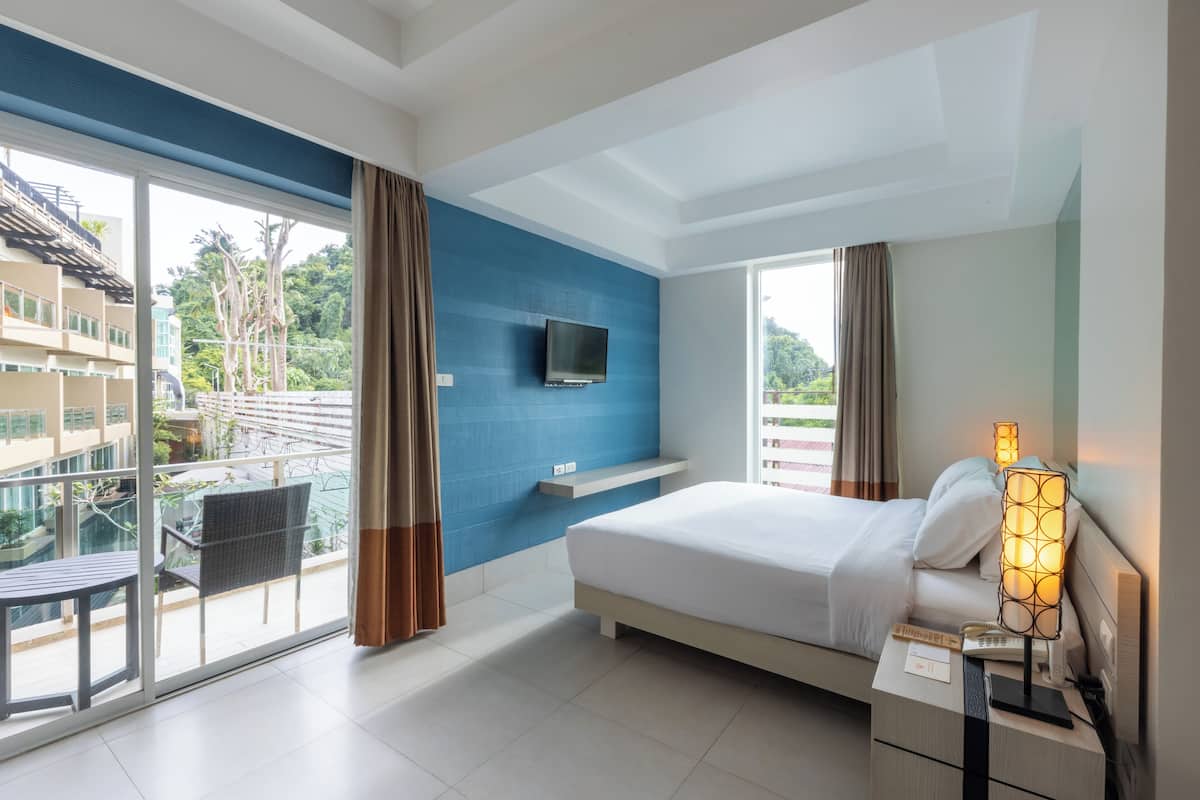 A hotel room with a large bed, a TV mounted on the wall, a bedside lamp, and a balcony with a table and chairs.