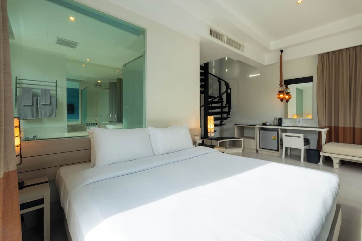 A hotel room with a large bed, a desk, a chair, a small refrigerator, and a mirror.