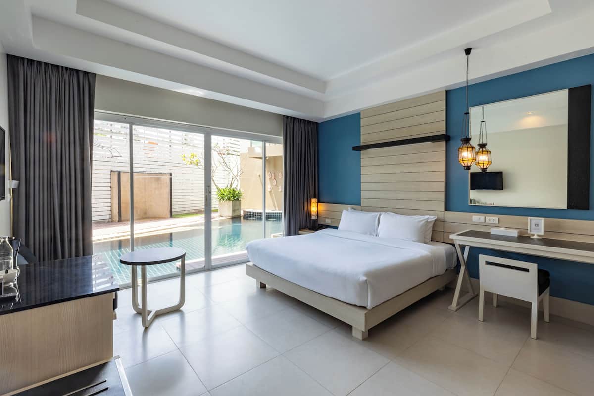 A modern hotel room with a large bed, a desk, and a view of a swimming pool.