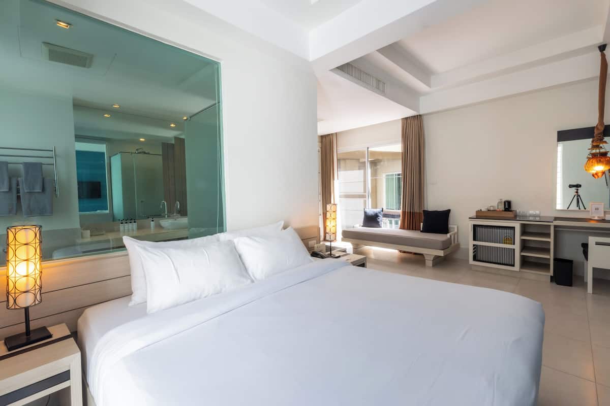 A modern hotel room with a large bed, a desk, a mirror, and a view of the city.