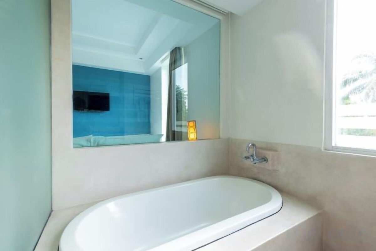 A modern bathroom with a freestanding bathtub, a large mirror, and a window providing natural light.