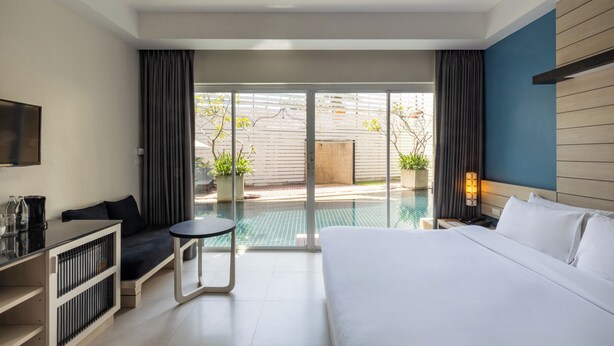 A hotel room with a bed, a small table, a sofa, a TV, and a view of an outdoor swimming pool. - Navinda Krabi (Krabi)