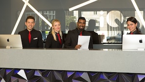 A reception desk with four individuals standing behind it, each with a laptop. - iQ Hotel Roma (Rome)